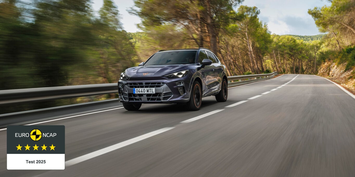 A dark grey Cupra Terramar SUV drives on a road, surrounded by green trees.