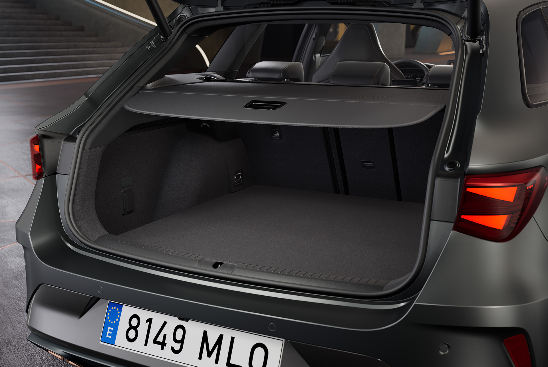 Open boot of a new grey Cupra Leon Sportstourer hybrid vehicle, revealing a spacious cargo area with a black interior. The boot holds a bag.