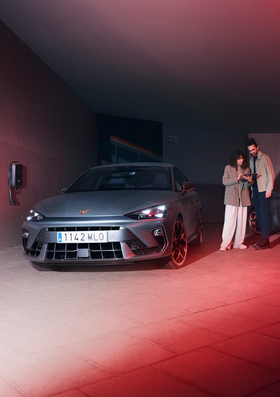 A sleek, matte grey CUPRA Leon Sportstourer 2025 is parked on a picturesque promenade at dusk. The car's rear side is highlighted, showcasing its sporty design. 