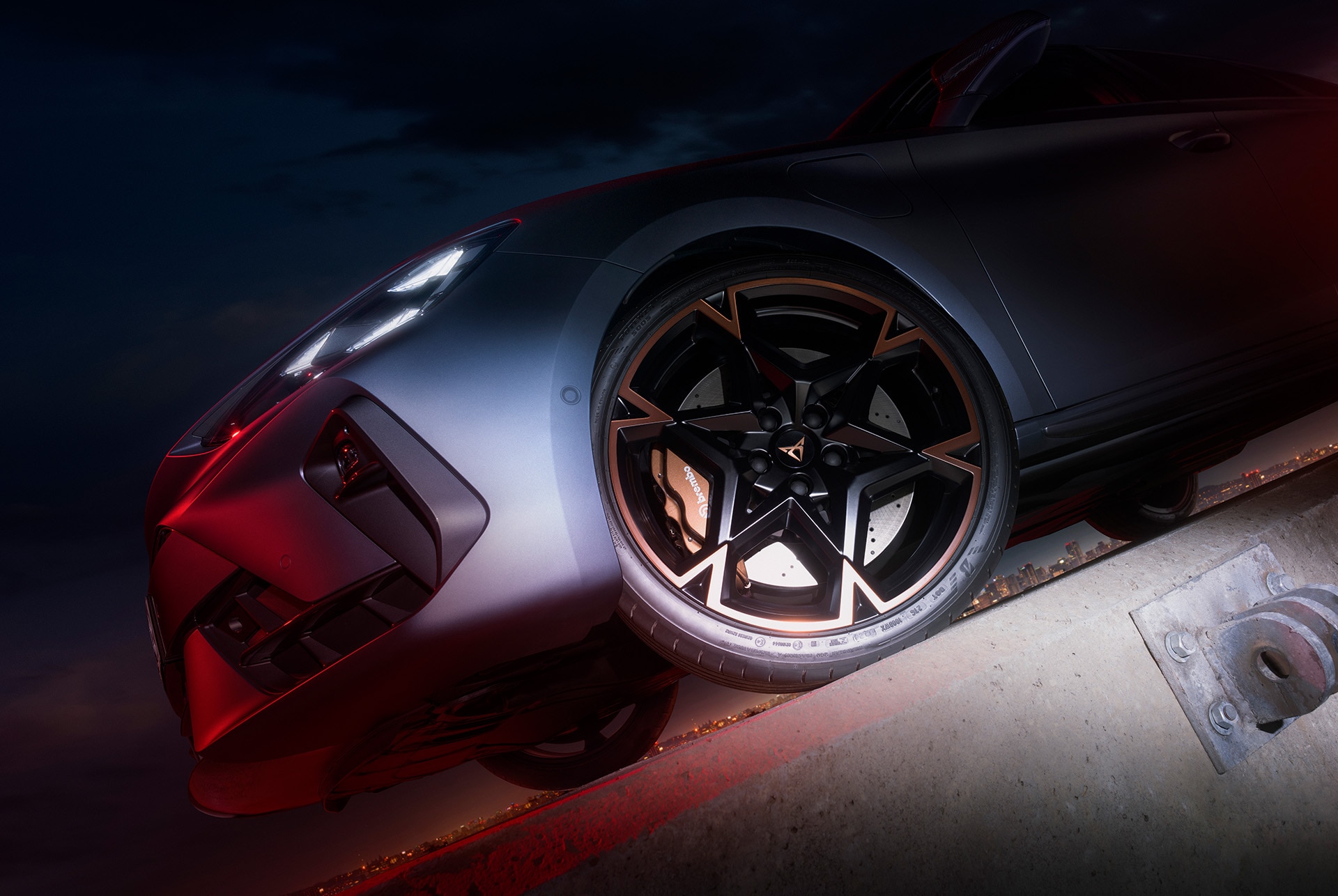 The image focuses on the front wheel and brake assembly of a matte grey CUPRA Leon. The wheel design is striking with a multi-spoke pattern and copper accents. The brake calipers are visible, painted in a matching copper color.