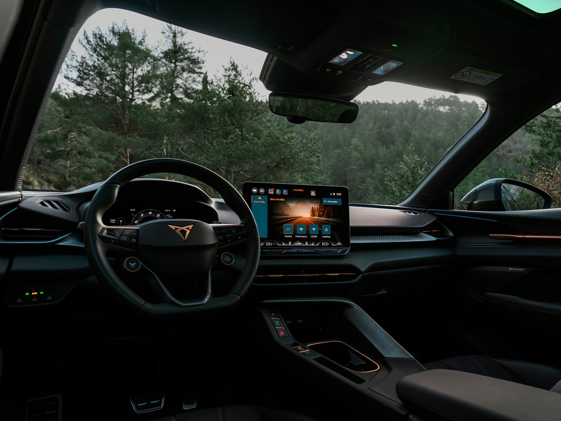 CUPRA Terramar’s interior shot, which highlights the dashboard with a driver-first design. The car is parked in an outdoors setting surrounded by trees.
