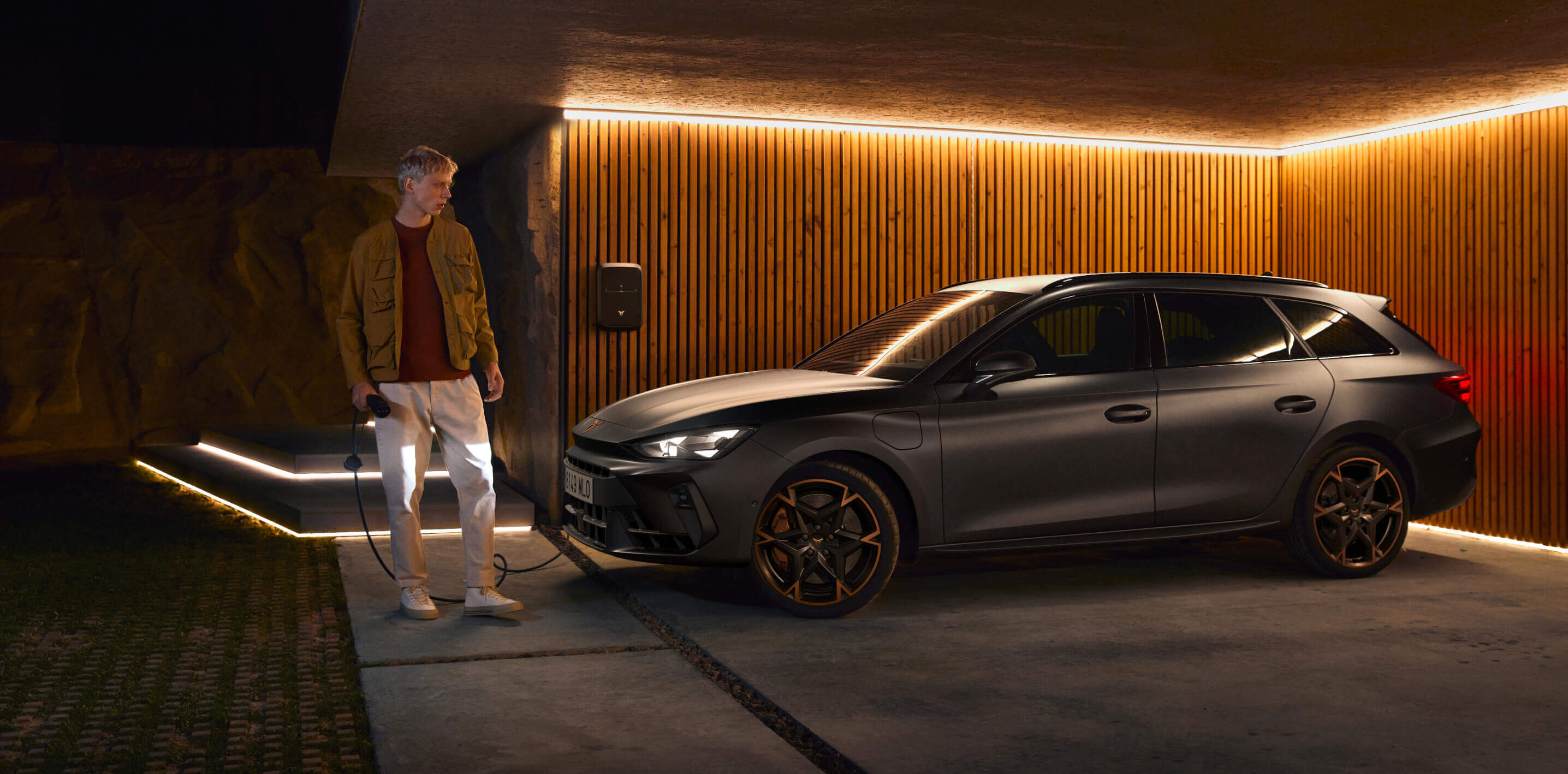 electric and hybrid car home charging in garage with wall charger installed, owner holding cable