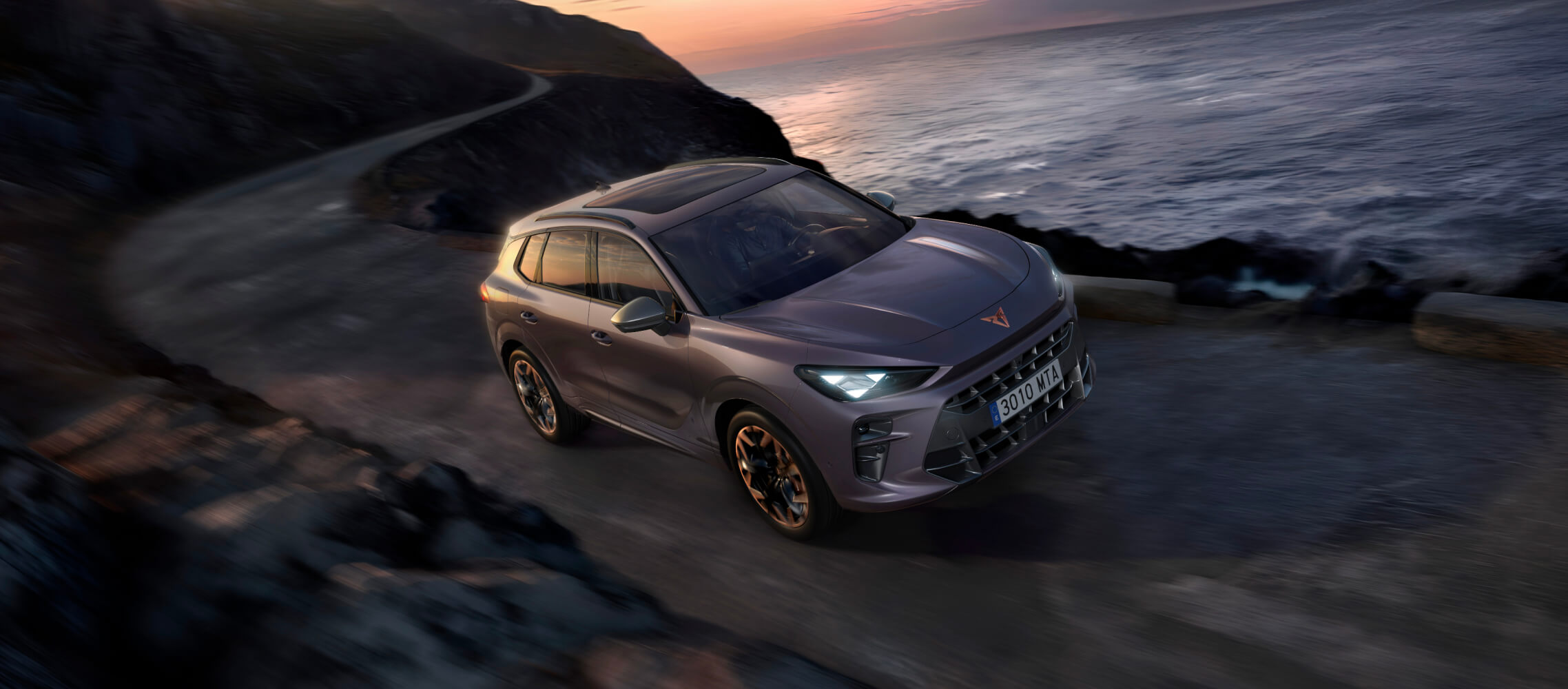 A terramar, electric car, driving through a rocky road, with the sea on one side and a colourful sunset on the background