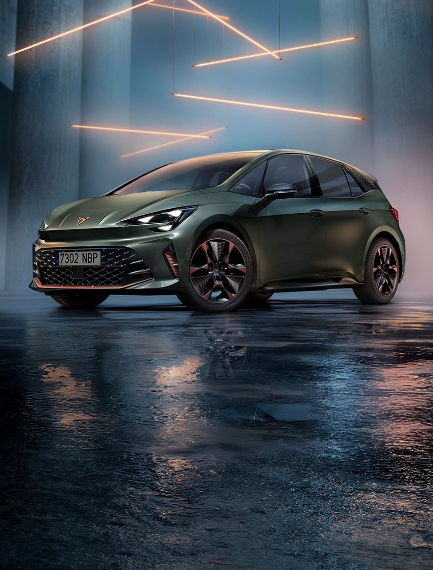 Front three-quarter view of a CUPRA Born in Dark Forest colour, parked in a minimalist concrete garage with a wet, reflective floor. The ceiling features horizontal linear metal lighting that illuminates the vehicle from above.